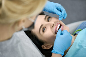 Happy girl in a patient's bib in a dental clinic. Dentist in blue latex gloves is flossing her teeth with a help of a dental floss. Closeup horizontal photo.
