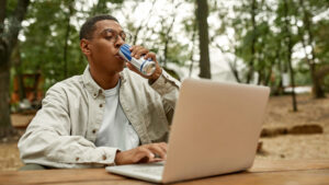 man drinking energy drink while working on laptop outdoors